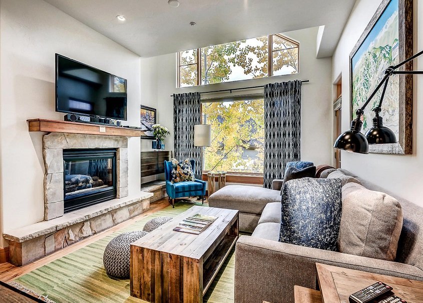 Beaver Creek cabin lounge with couches, coffee table, tv, fireplace and large window looking out onto tree tops.