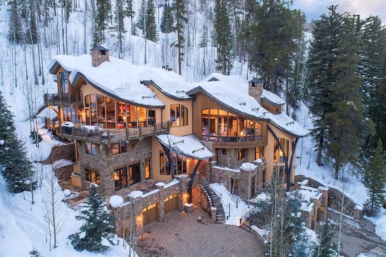 Aerial view of Vail ski-in/ ski-out rental option nestled in a snowy forest, warmly lit with artistically curved windows.