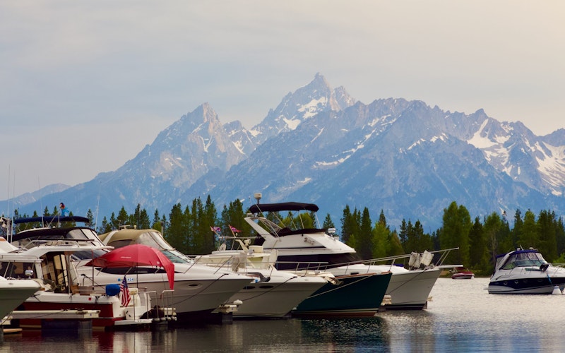 Boats on a lake with trees and snowy mountains in the background at Jackson Hole.