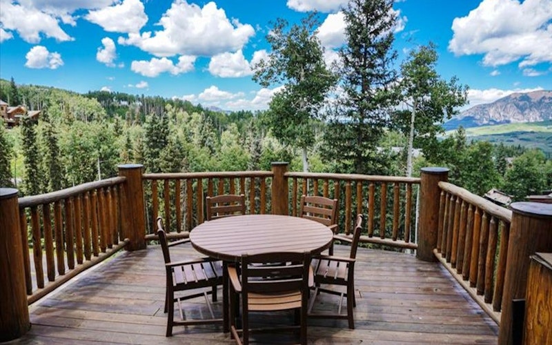 Wooden patio and table overlooking valley with many trees at a Telluride vacation rental.