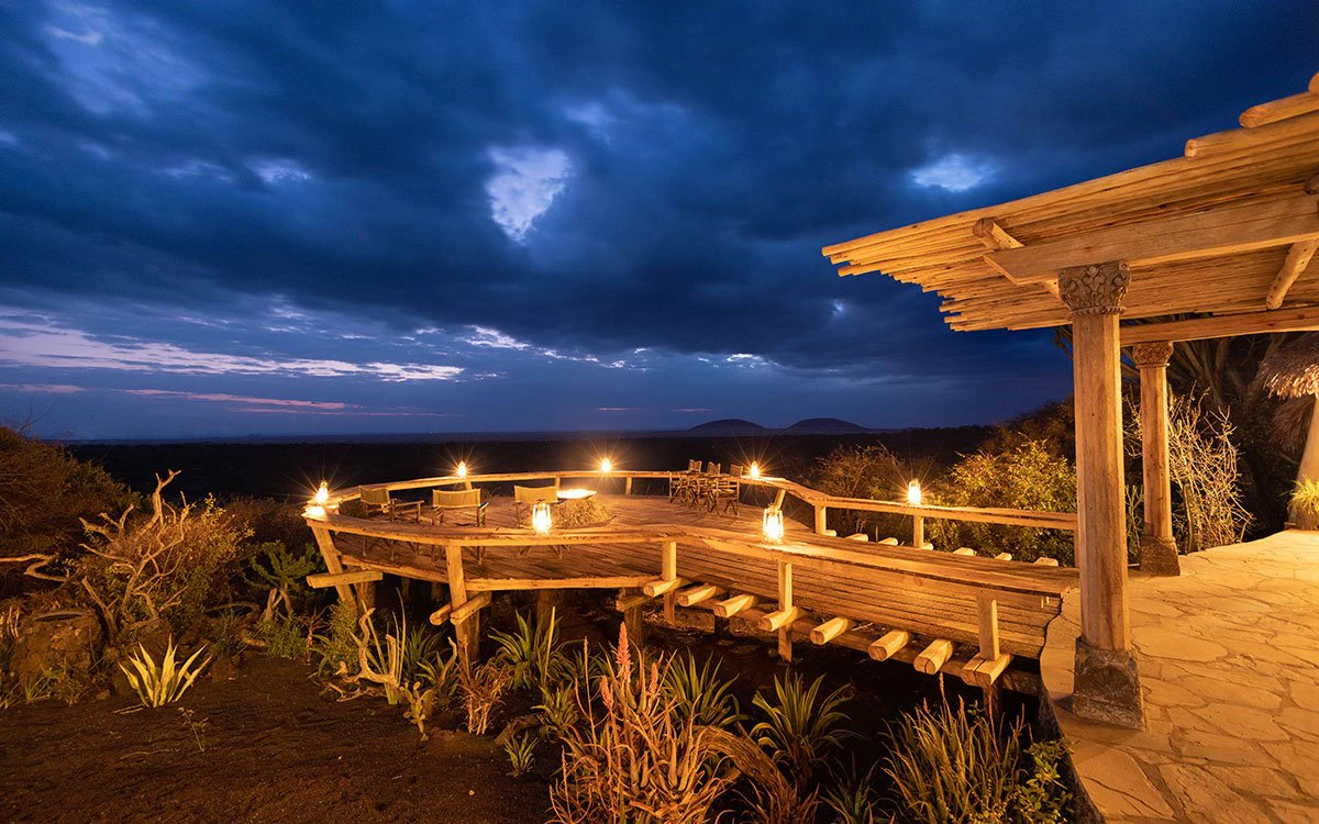 A beautifully lit up outdoor deck with chairs with a moody, cloud-covered night sky above