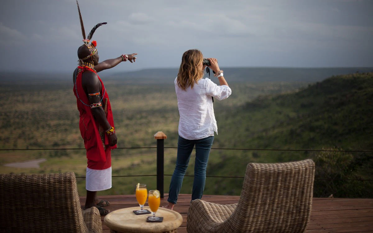 A guest peers out from the main deck at Loisaba Tented Camp under the watchful gaze of a local guide
