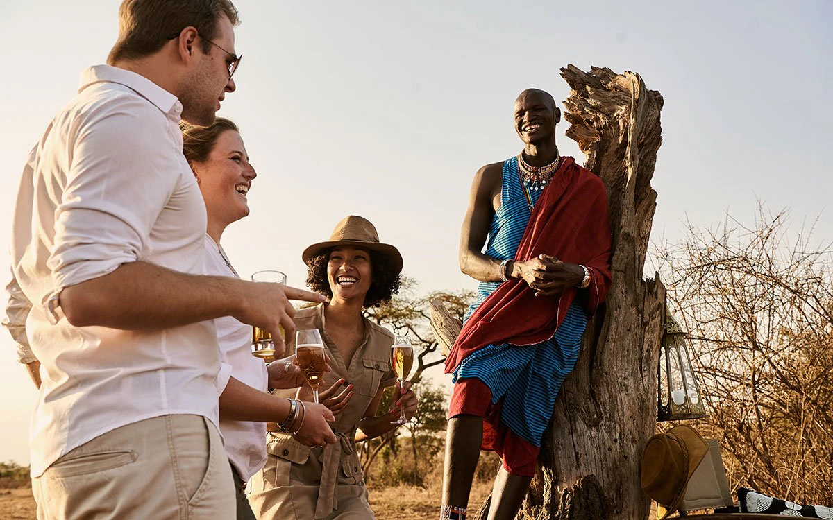 A group of safari guests and their guide enjoy a joke while sipping drinks during sundowners