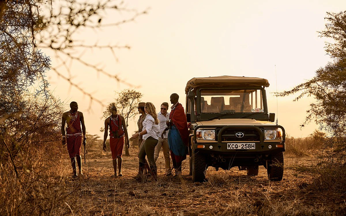 A group of guests take a break from their game drive to walk with their guides as the sun begins to set