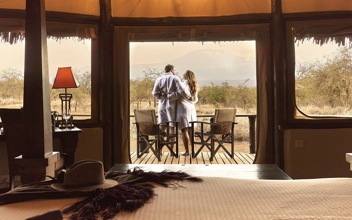 A couple on a safari vacation embrace in their bathrooms while standing on their private deck at Tawi Lodge