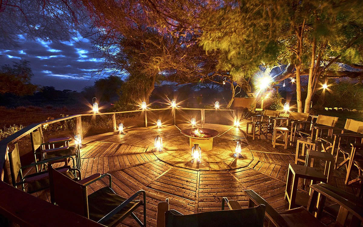 A beautifully lit outdoor deck at Tawi Lodge with a fire pit in the center and a dark, cloudy sky in the background