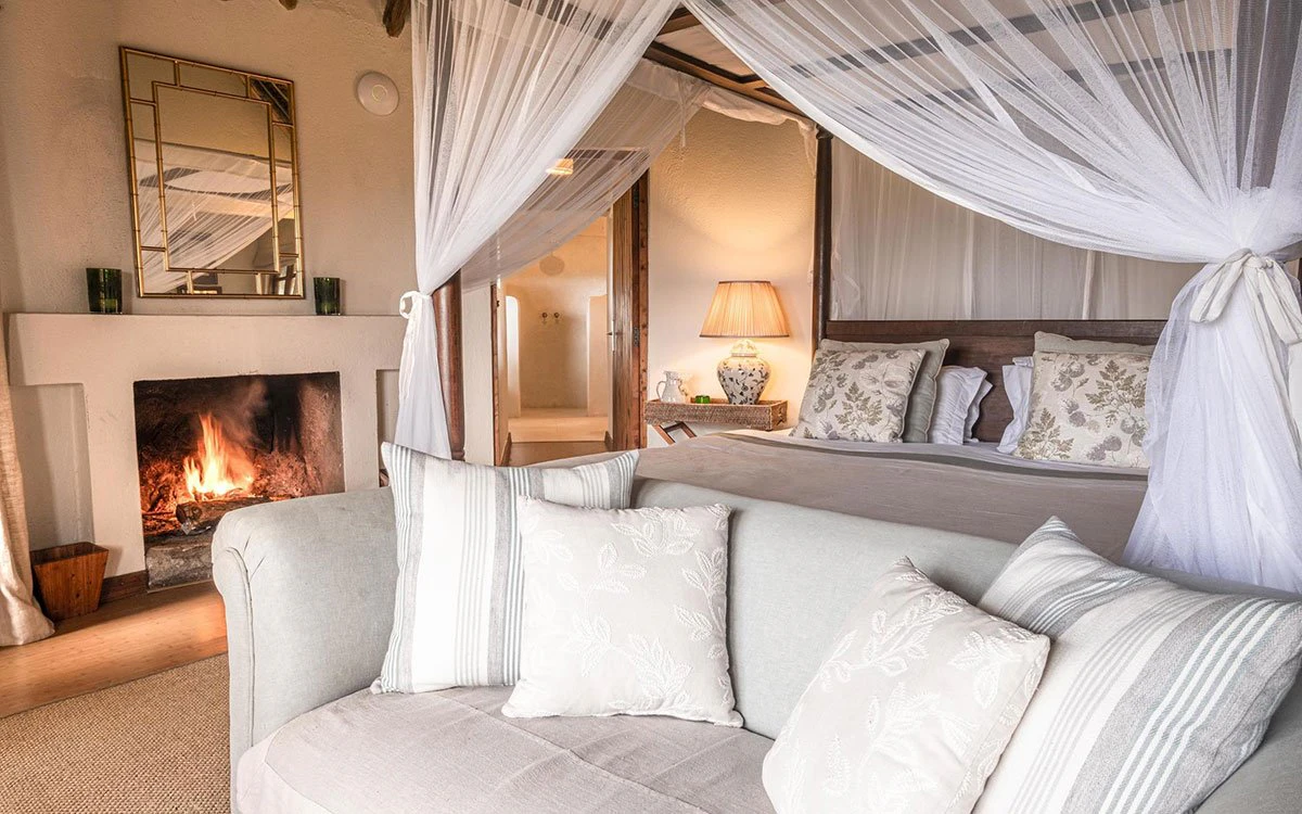 Internal image of one of the bedrooms at Loldia with the 4 poster bed and comfy seating in view and a roaring fire in the background