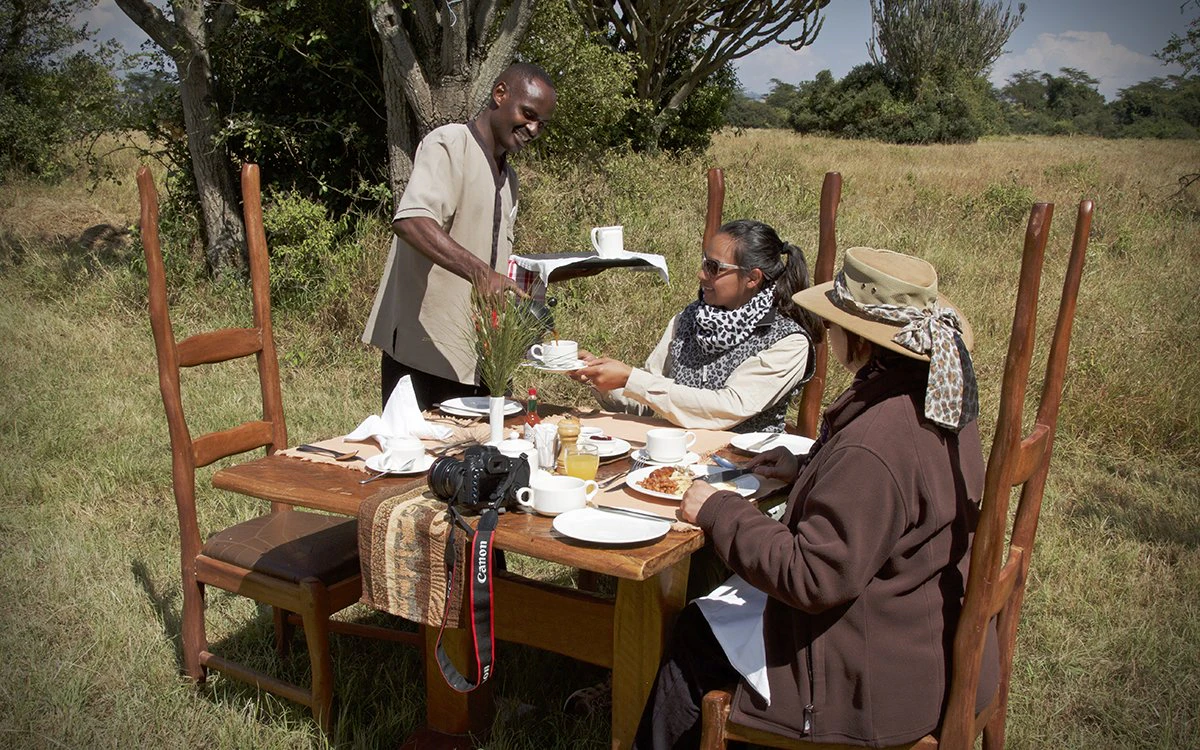 Two guests are served an al fresco breakfast near Mbweha Camp