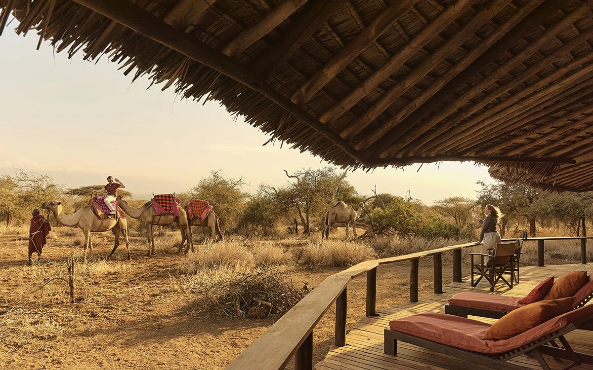 A male guest prepares to embark on a camel ride safari with a guide, while his female companion watches on from the private deck