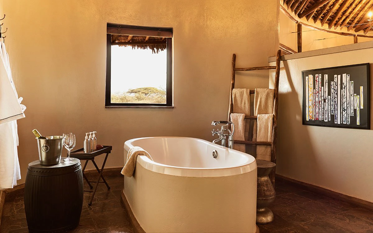 An empty tub inside an en suite bathroom at Tawi Lodge sits invitingly, with a bottle of wine nearby
