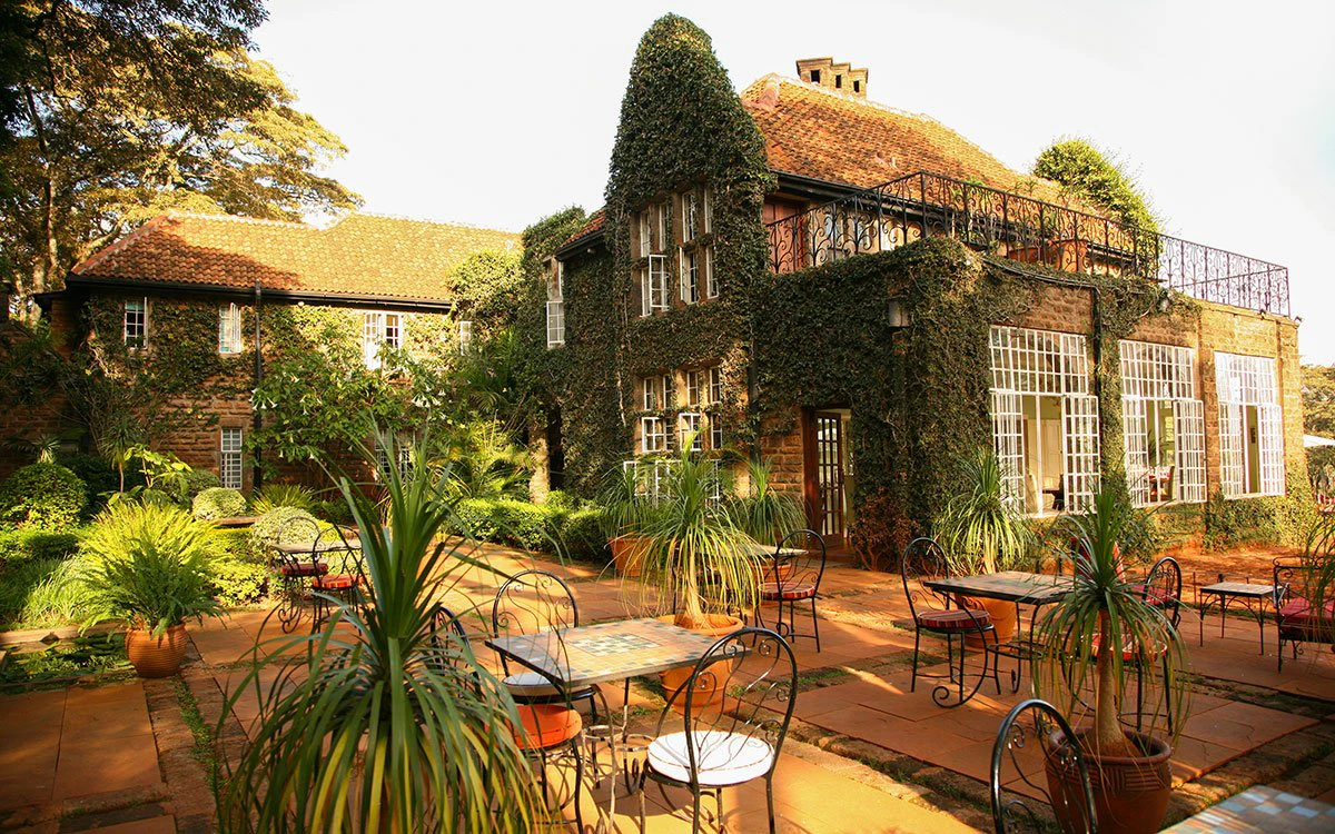 Exterior of Giraffe Manor adorned with vines, with an outdoor dining area in the foreground