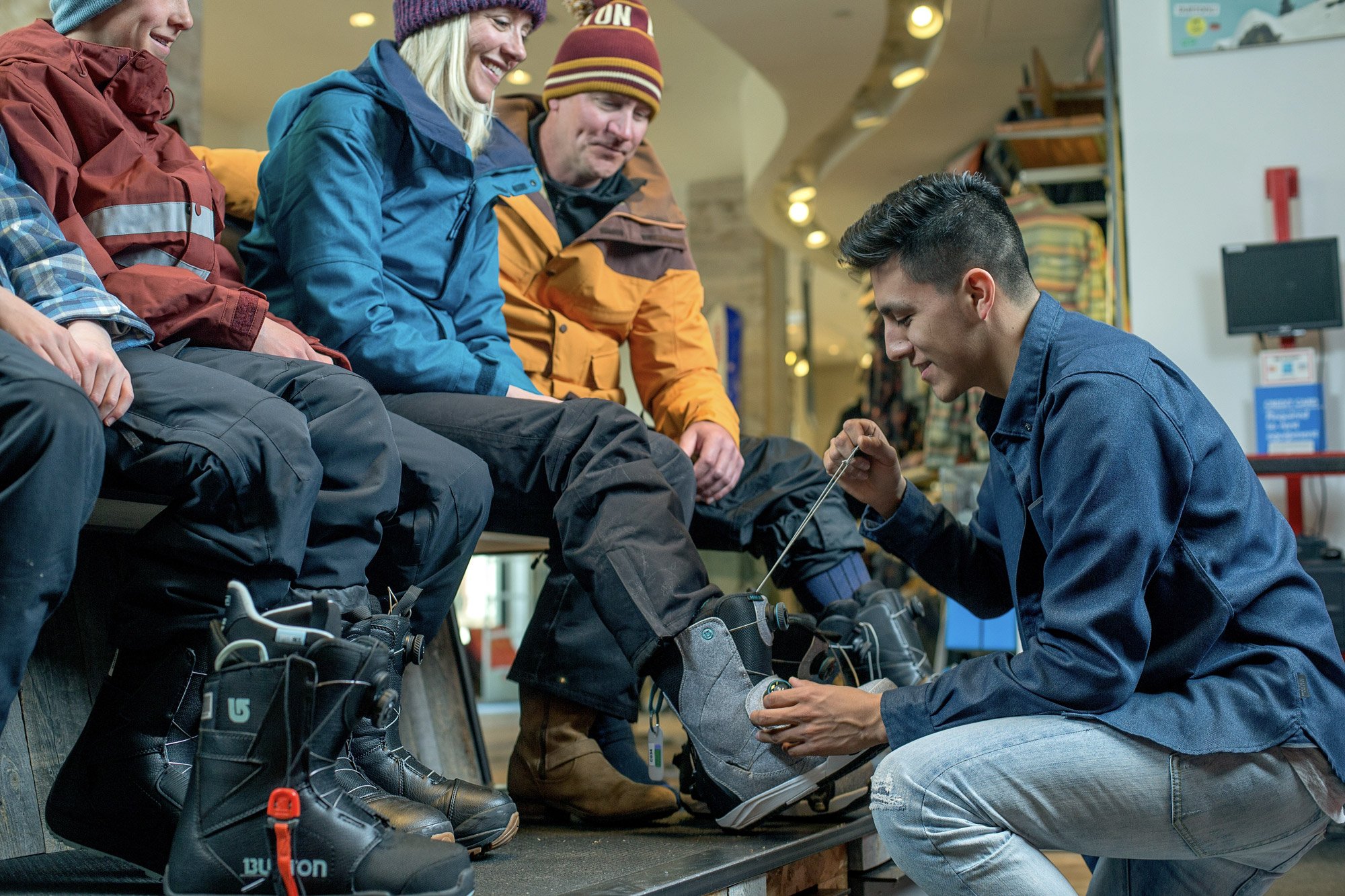 A group of snowboarders at a luxurious Vail equipment rental shop having their boots fitted.