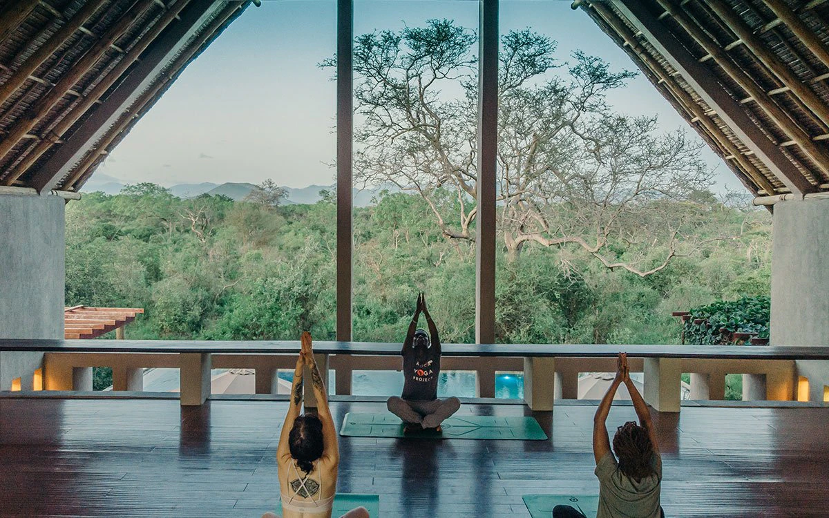 A pair of guests take part in a yoga session with an experienced trainer and a gorgeous view in the background