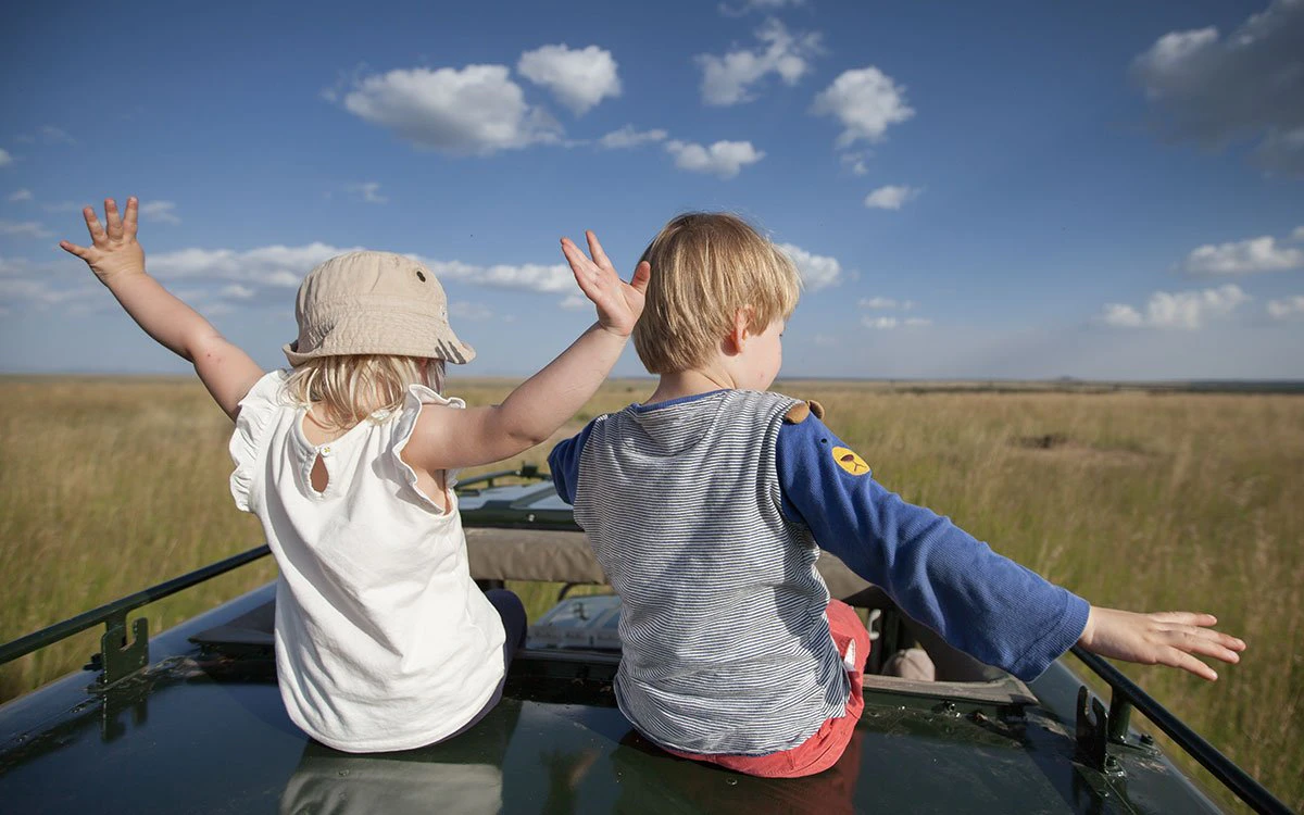 Two children enjoy a game drive on a blue sky day from Rekero Camp