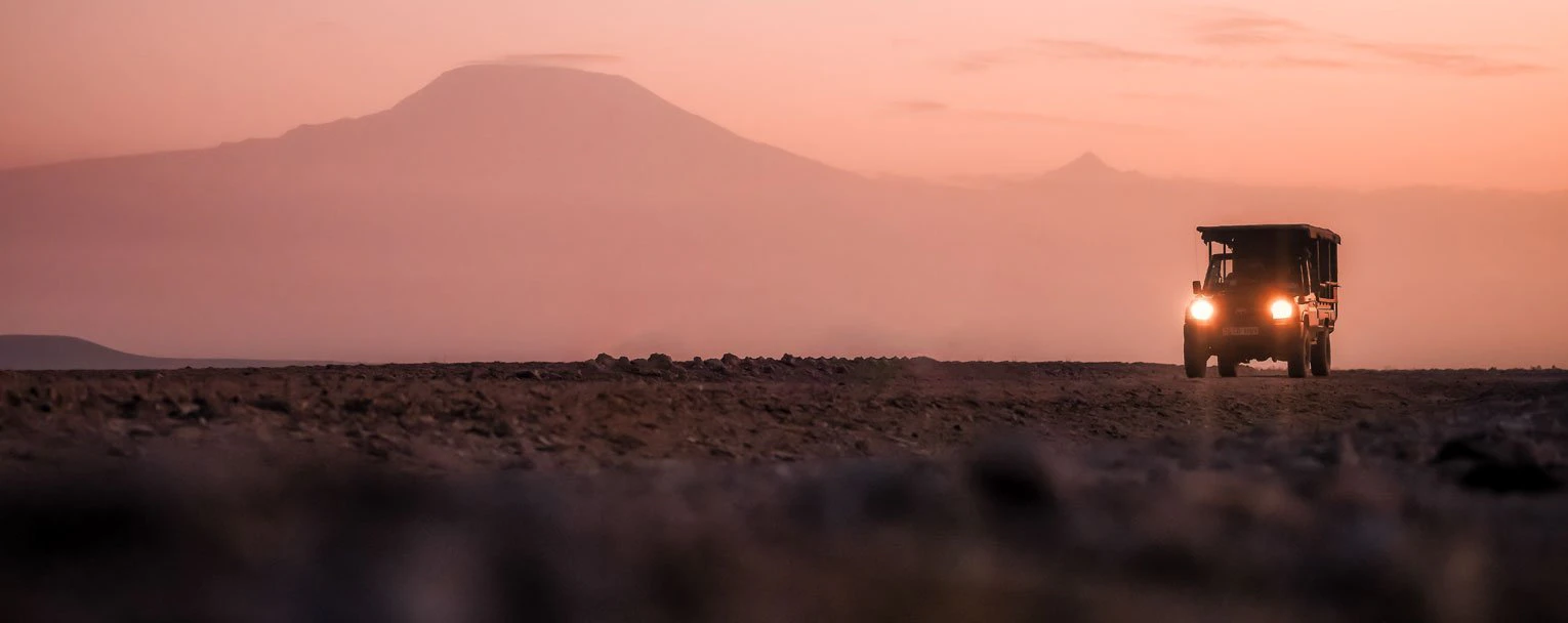 A vehicle embarks on a night drive at sunset with hazy mountains in the background A vehicle embarks on a night drive at sunset with hazy mountains in the background