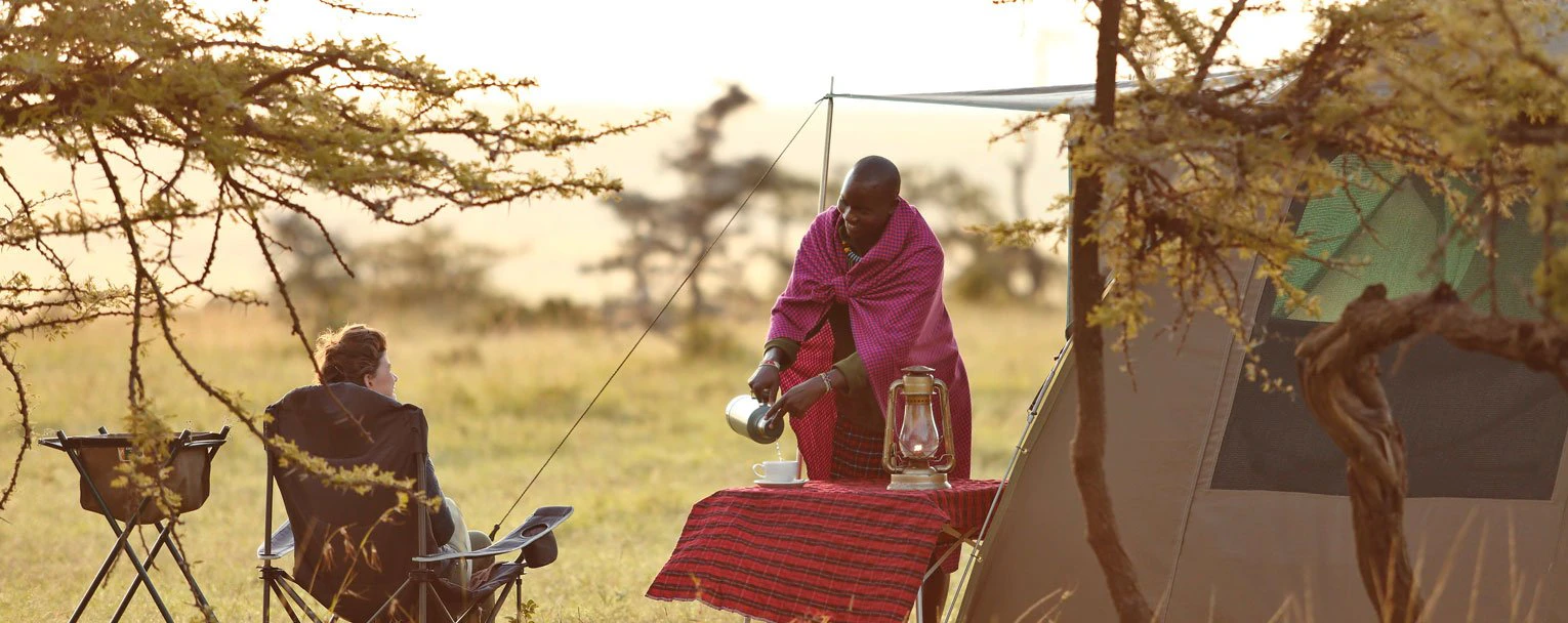 A guest relaxes as a member of staff sets up a fly camping tent