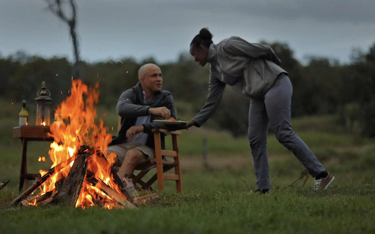 A guest is served snacks from a member of the Ol Pejeta team with a roaring fire in the foreground