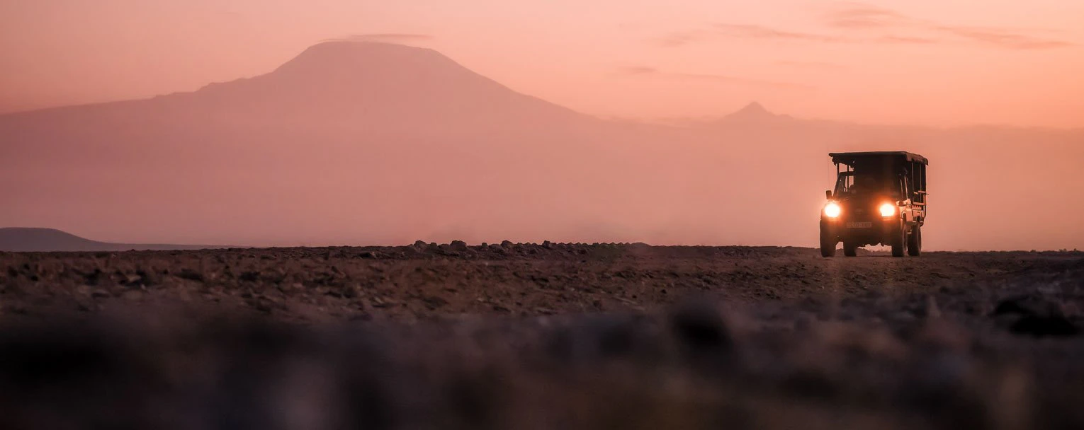 A safari vehicle heading out for a night drive with a hazy mountain backdrop