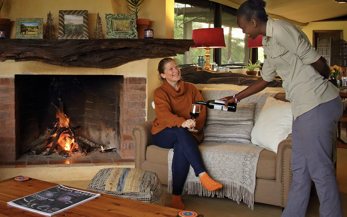 A guest at Ol Pejeta has a glass of wine poured for her in the communal living space