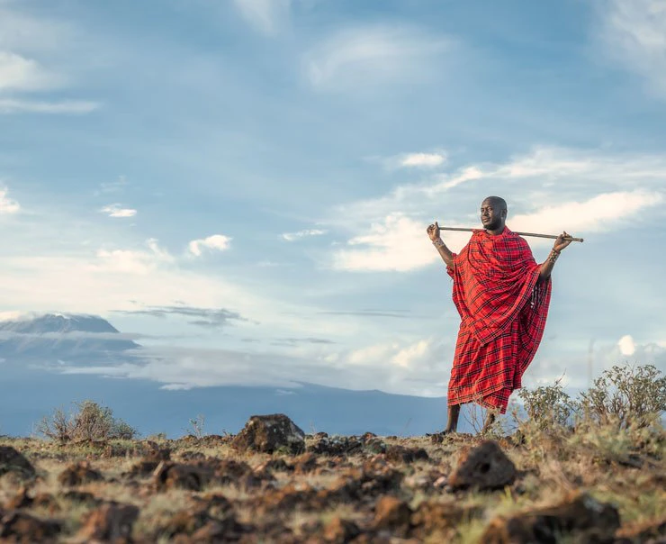 A Maasai guide surveys his surroundings with cloudy hills in the background