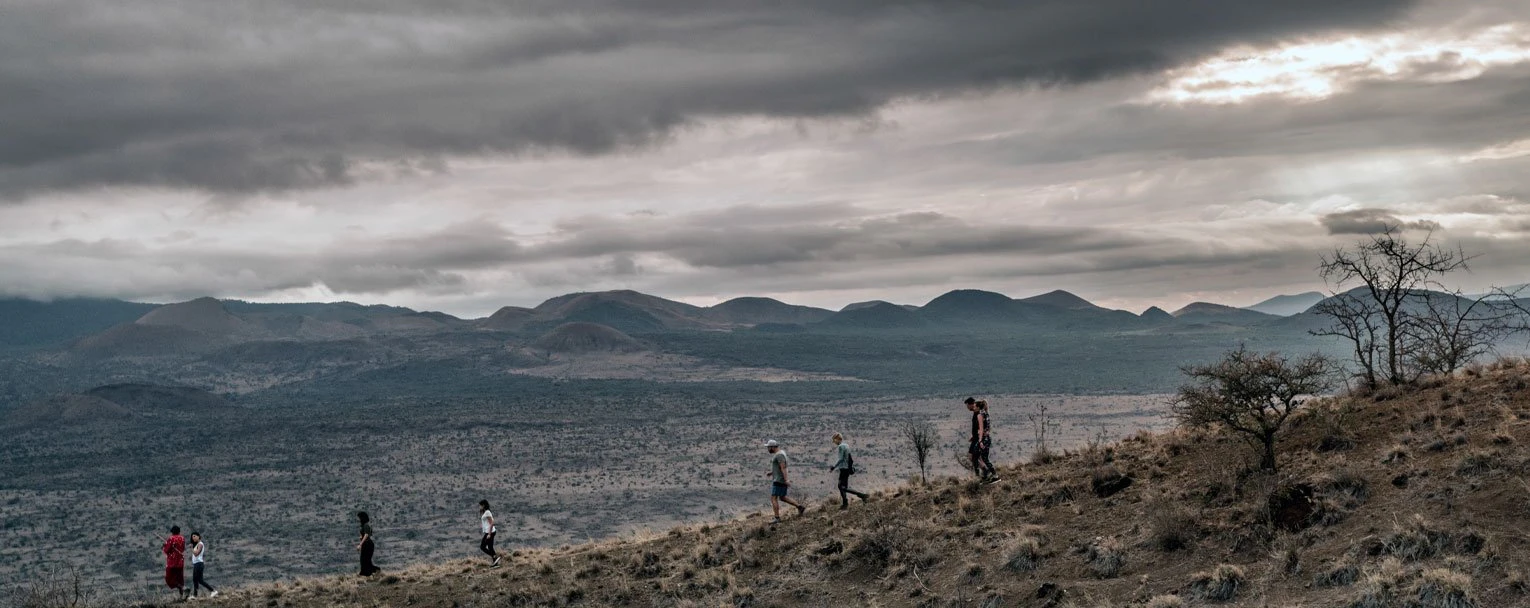 A group of guests out on a walking safari, with a gloomy, mountainous backdrop