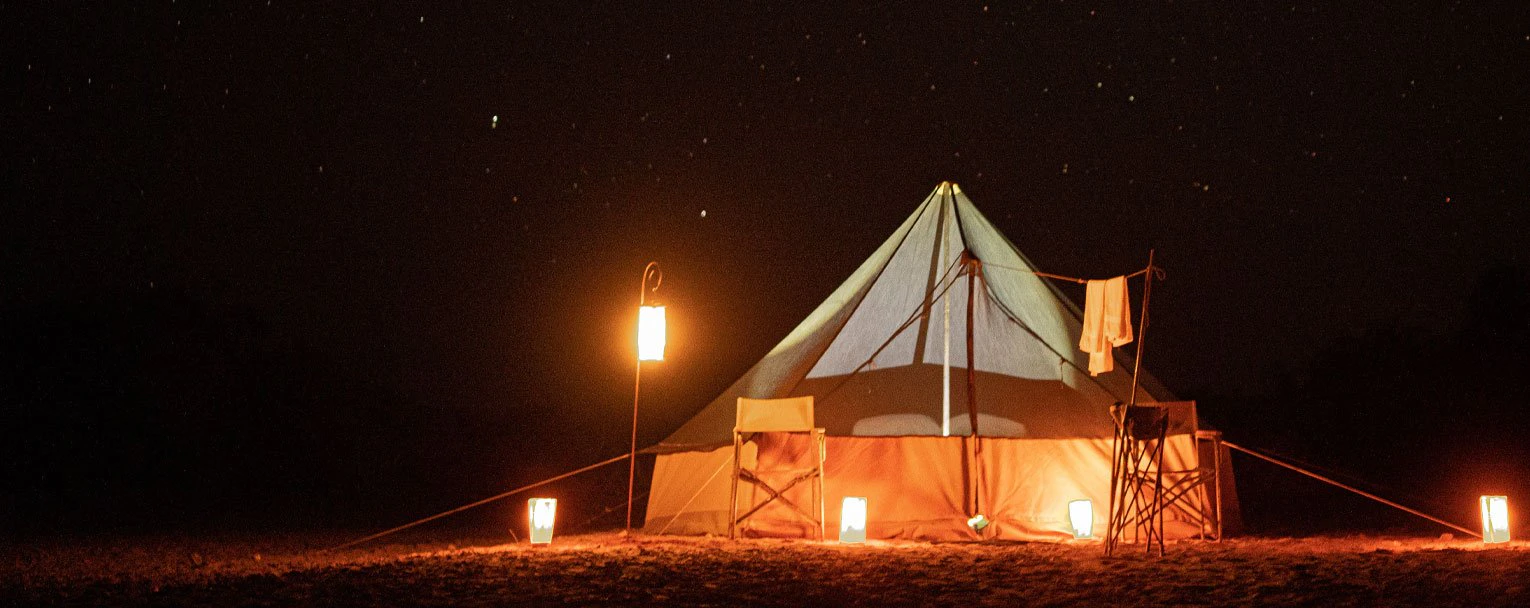 A beautifully lit up fly camping tent with a pitch back night sky in the background