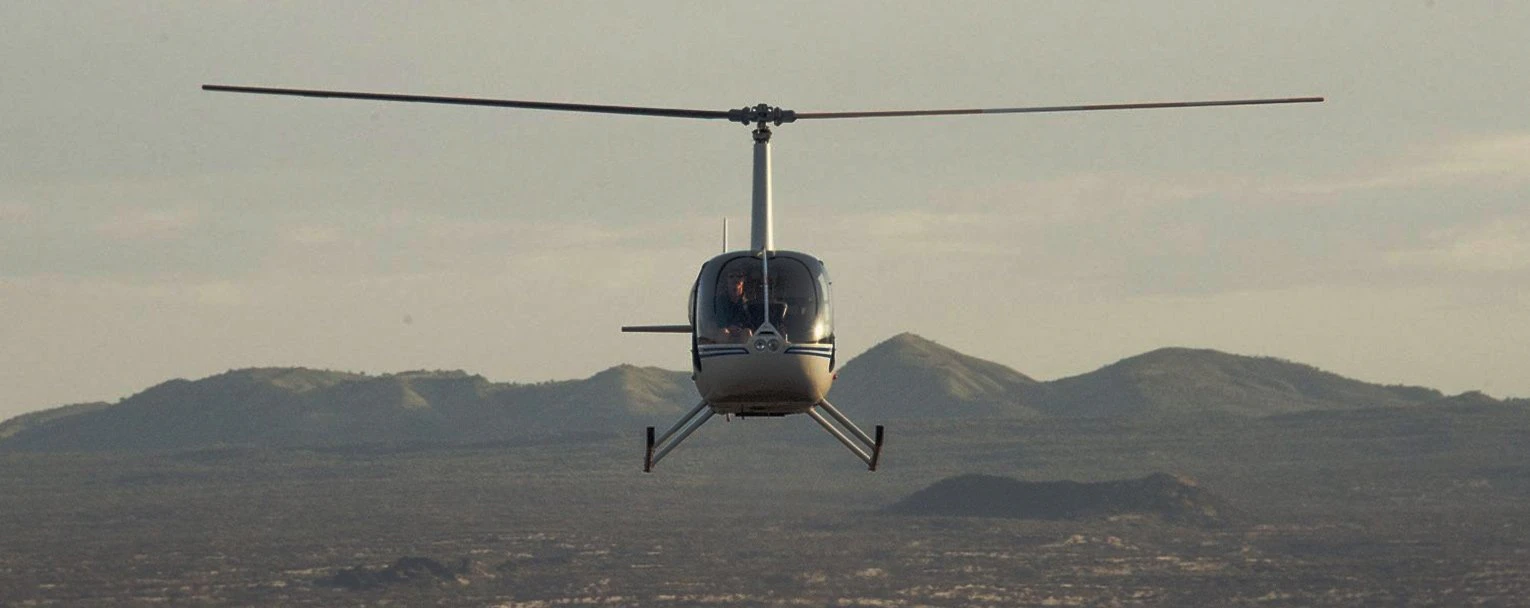 A helicopter flies toward the camera with a mountain background and hazy skies behind
