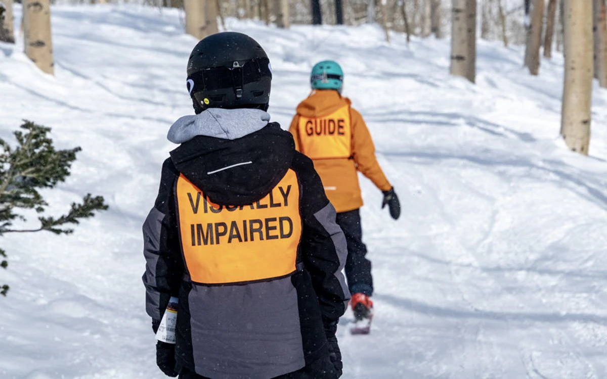 A visually impaired skier and their instructor make their way down the mountain.