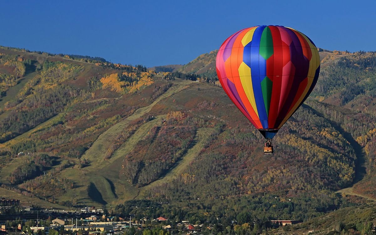 A hot air balloon soars through the summer sky with the mountains in the background.