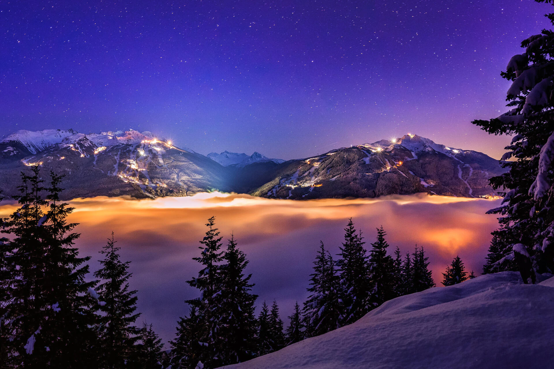 Whistler and Blackcomb mountains lit up in the background on a dark, cloudy winter’s night.