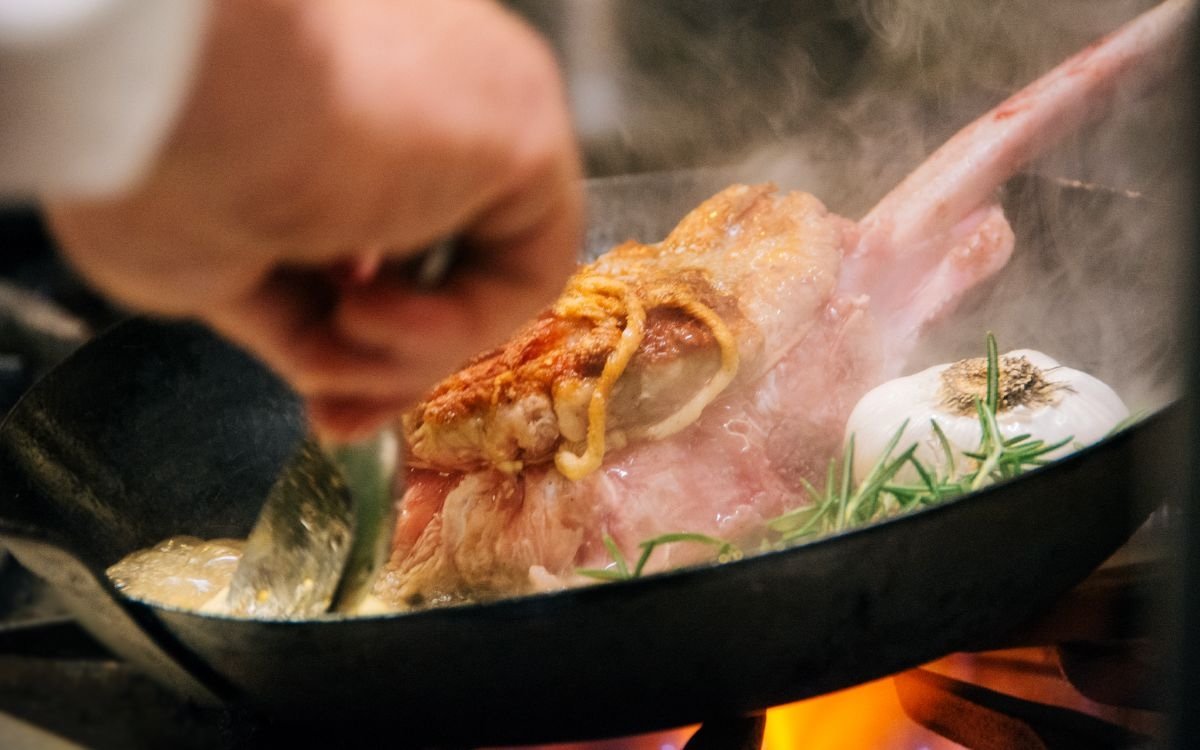 A steak is sizzling in a pan in the kitchen at Apex Restaurant in the Montage.