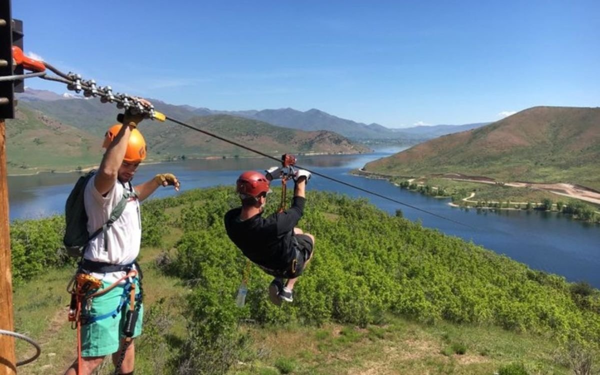 A pair of friends enjoy an exhilarating zipline with the mountains and lake in the background.