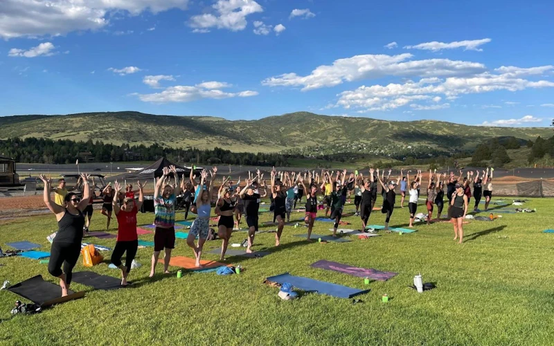 A group outdoor yoga session takes place against a beautiful summer backdrop.