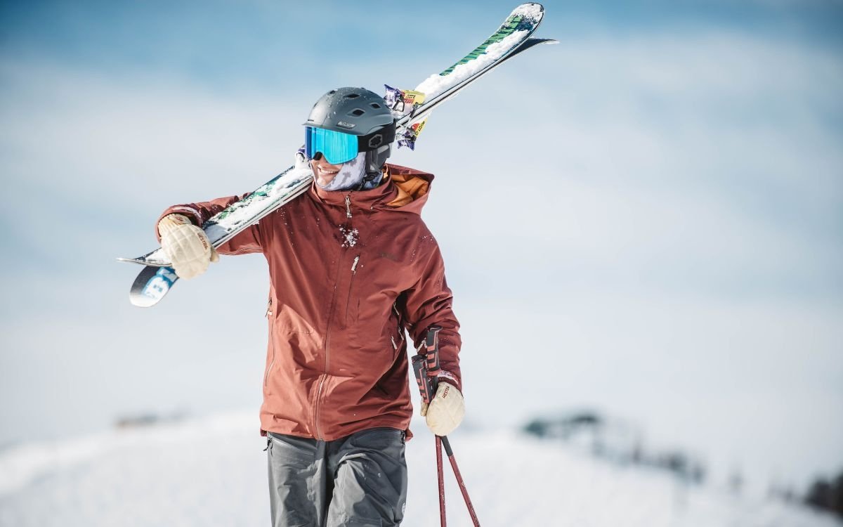 A single skier carries a pair of skis on his shoulders as he begins his day on the slopes.