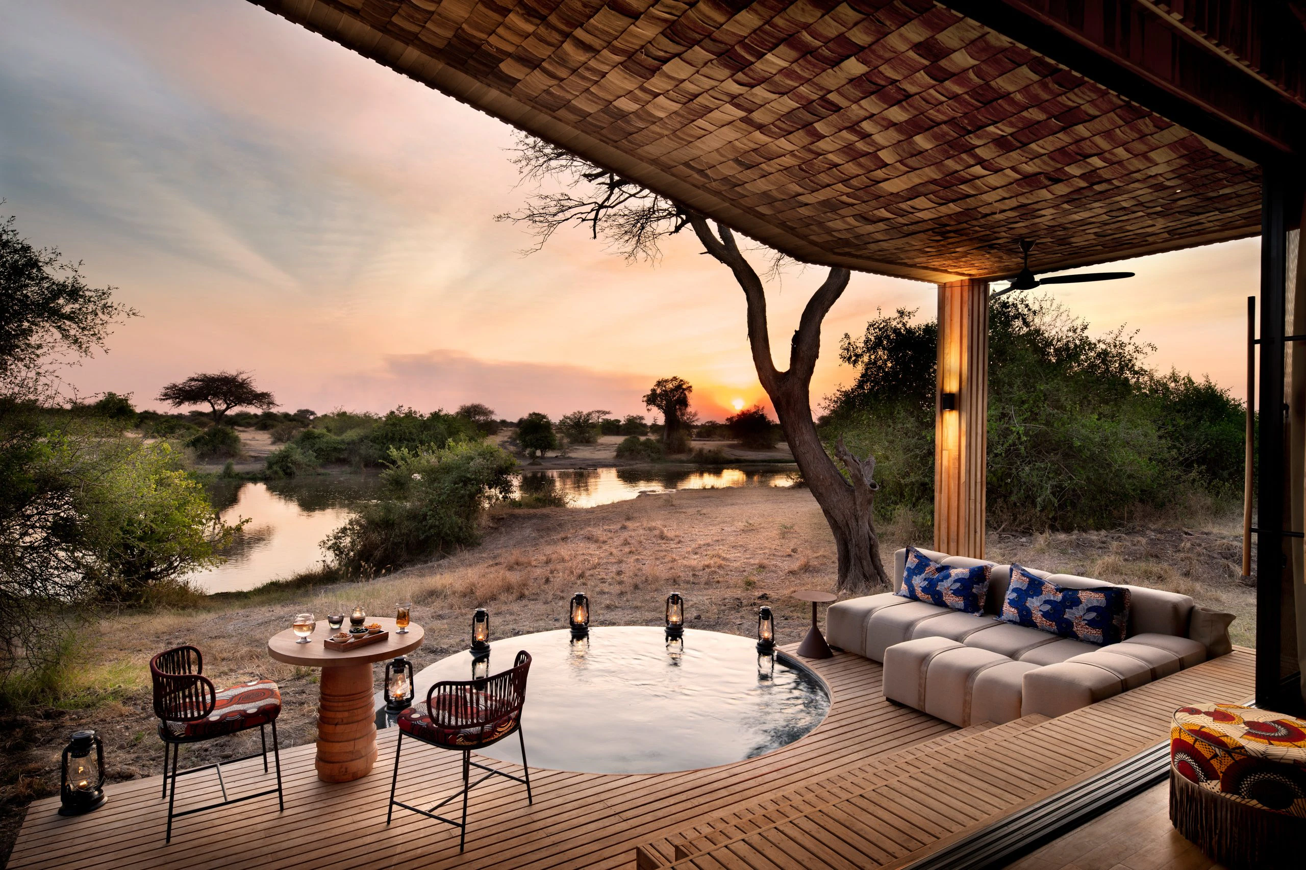 Luxury safari lodge deck overlooking a river at sunset, featuring a private plunge pool, lanterns, and elegant outdoor seating in the African wilderness. Luxury safari lodge deck overlooking a river at sunset, featuring a private plunge pool, lanterns, and elegant outdoor seating in the African wilderness.