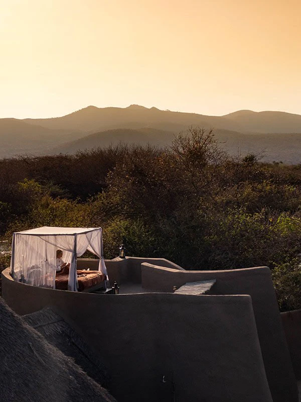 Guest relaxing on a romantic outdoor star bed under a mosquito net at sunset, overlooking the African wilderness during a luxury honeymoon safari.