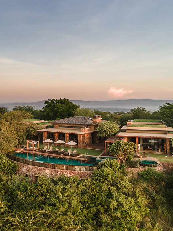Aerial view of a luxury safari lodge in Tanzania featuring a cliffside infinity pool, elegant suites, and panoramic views over the savannah at sunset.