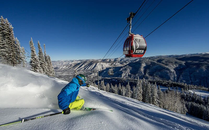 Skier descending snowy slopes with gondola overhead at Aspen resort—highlighting winter activities available with Aspen luxury vacation rentals. Skier descending snowy slopes with gondola overhead at Aspen resort—highlighting winter activities available with Aspen luxury vacation rentals.