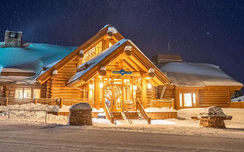 Log cabin with glowing lights and snowy setting, showcasing the rustic elegance of Big Sky luxury rentals. Log cabin with glowing lights and snowy setting, showcasing the rustic elegance of Big Sky luxury rentals.