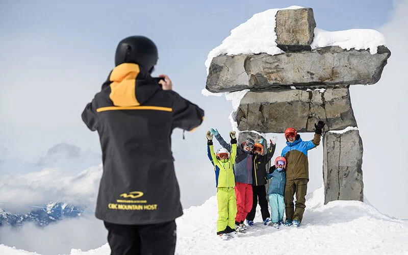 Family and ski instructor in front of Inukshuk statue on Whistler Mountain, showing family-friendly amenities offered by Whistler Luxury Rentals.