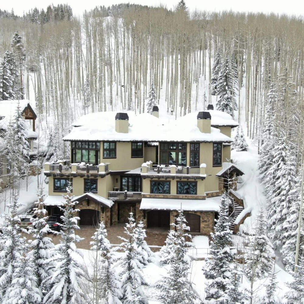 Luxury Vail ski-in/ski-out mountain chalet surrounded by snow-covered pine forest and winter landscape.