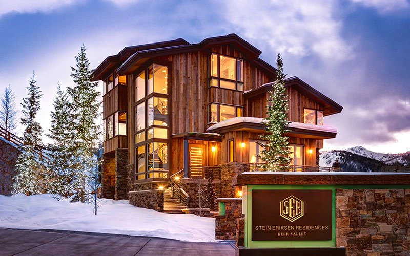 Exterior of Stein Eriksen Lodge in Deer Valley with snowy trees and warm lighting, highlighting luxury Deer Valley ski-in/ski-out accommodations.