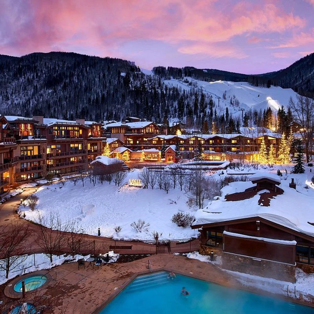 vail-condos-manor-lodge-intro Twilight view of Manor Vail Lodge with lit windows and snow-covered grounds, showcasing the charm of these high-end Vail Condos.