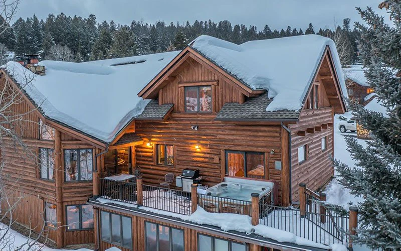 Rustic log-cabin exterior of Blue Grouse, a family-friendly option among Big Sky Condos with hot tub and snow-covered roof.