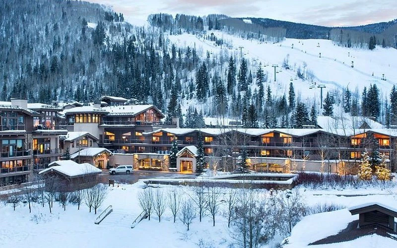 Snowy twilight view of Manor Vail Lodge, a top-rated Vail Condo with pools and spa amenities, shown next to “Your Guide to Vail’s Best Condo Stays.”