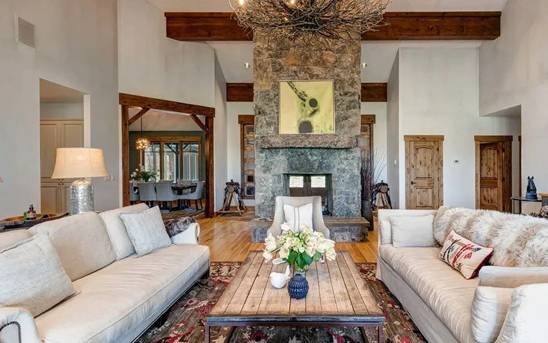 Open Meadows Jackson Hole Vacation Rentals elegant living room with stone fireplace, wood beams, and comfortable mountain décor.