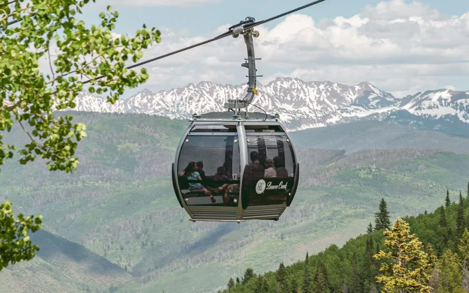 Beaver Creek summer gondola, mountain sightseeing access Beaver Creek summer gondola carrying sightseers up the mountain, with green forested slopes and the snow-capped Colorado Rockies in the distance