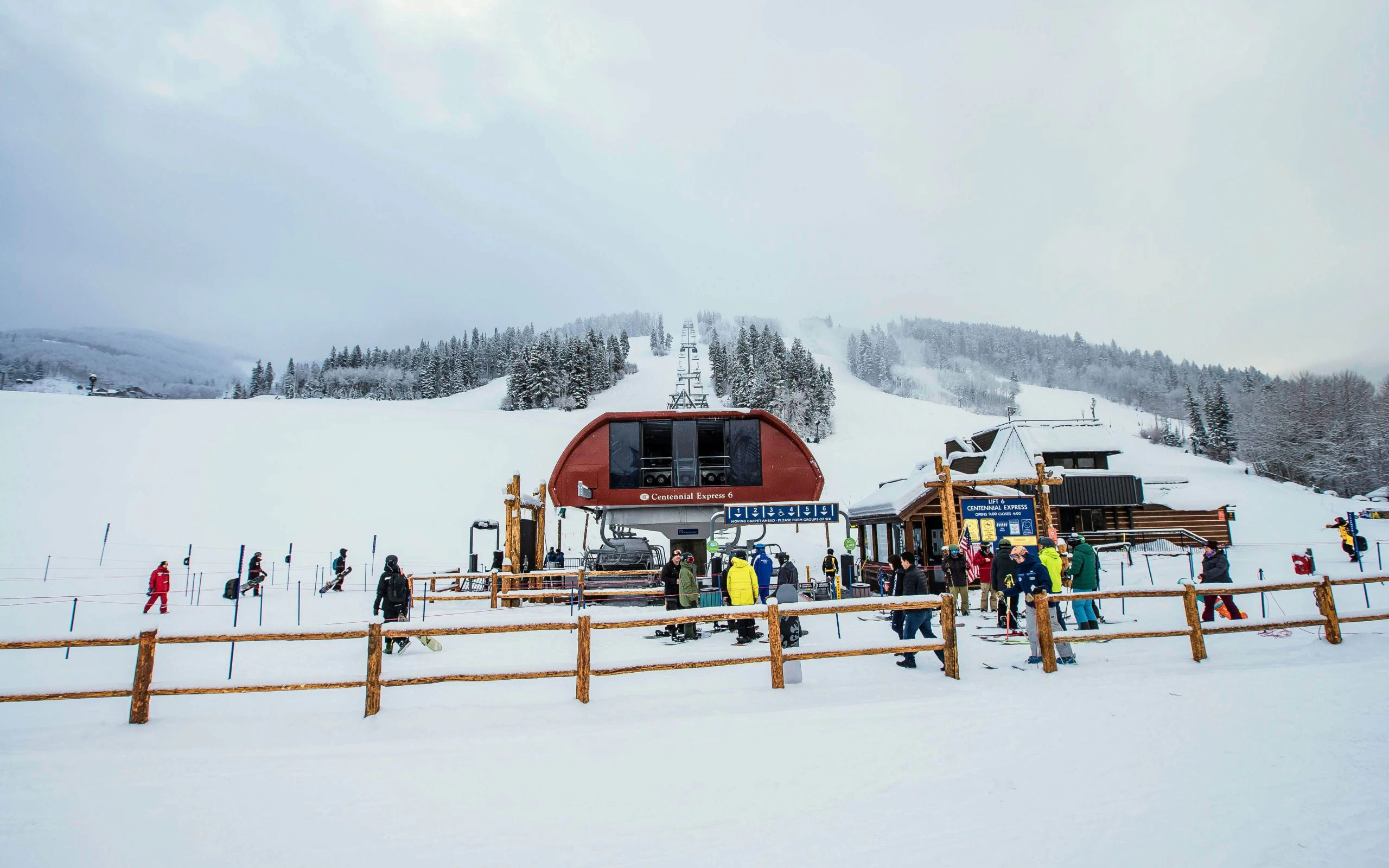 Skiers and snowboarders gathering at the base of the Centennial Express 6 lift below Beaver Creek's snow-covered slopes