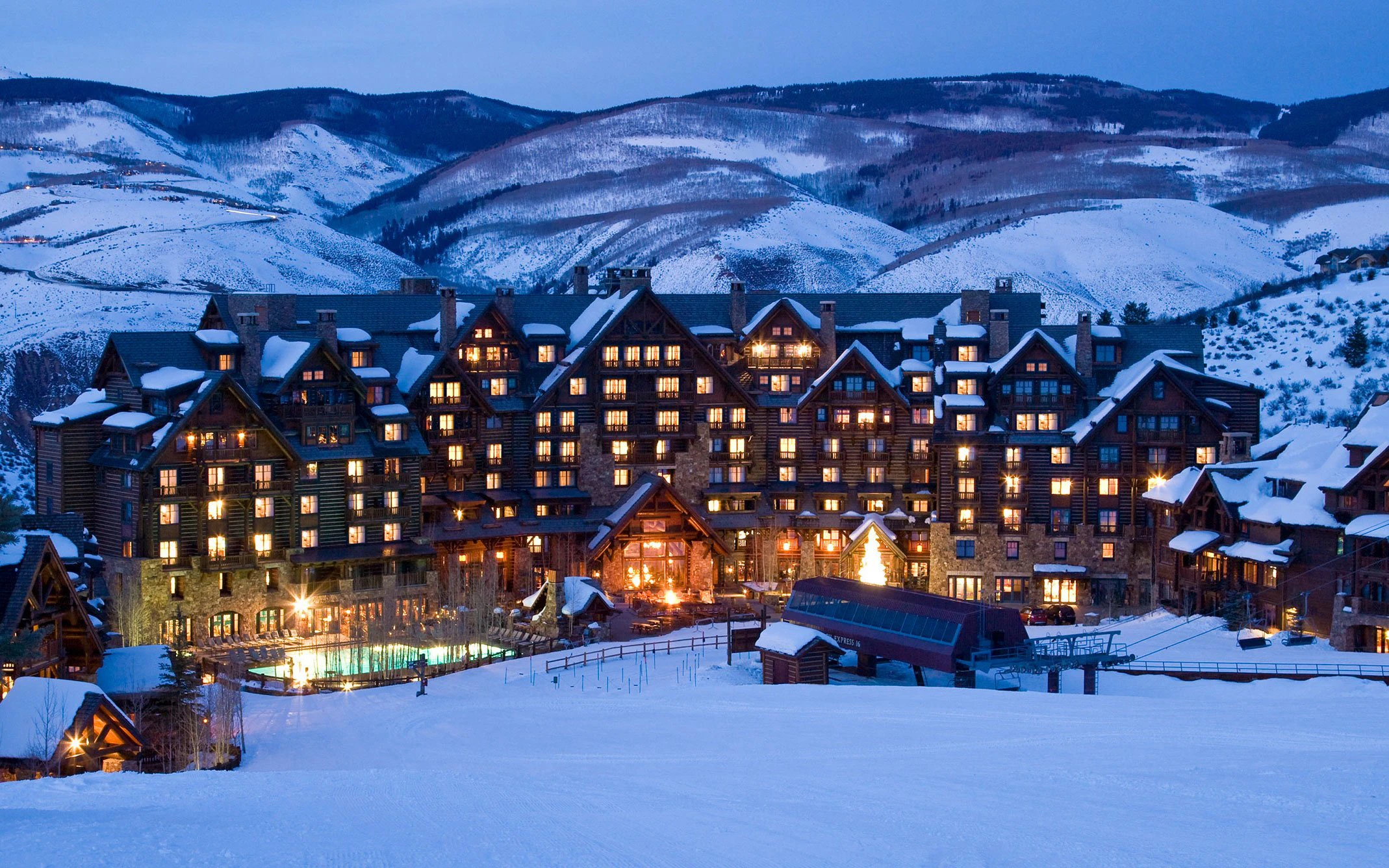 The Ritz-Carlton, Bachelor Gulch lit up at dusk, the timber lodge at the heart of Bachelor Gulch Village in Beaver Creek, with fresh snow and the mountains behind