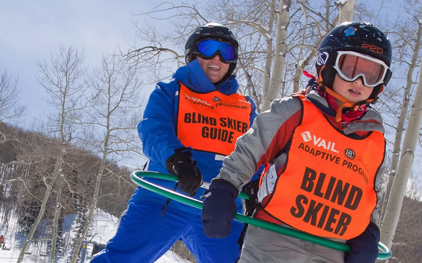 Adaptive skiing and snowboarding, Beaver Creek Beaver Creek adaptive skiing lesson, a Vail Adaptive Program guide skiing alongside a blind skier connected by a guide bar on a snowy aspen-lined slope